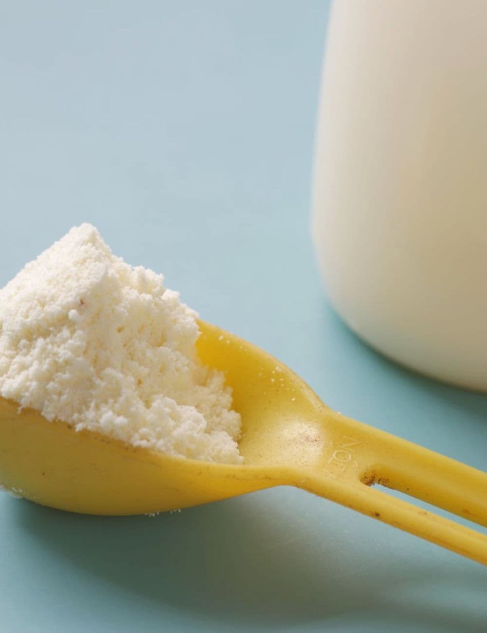 Milk powder measured from a scoop beside a bottle